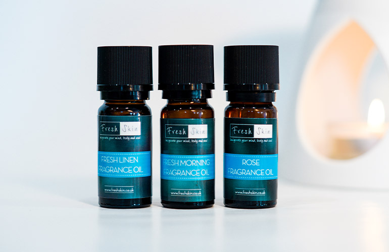 Three glass bottles of fragrance oil with candle in background